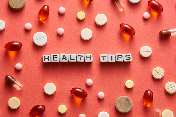 Zwart-wit titel gezondheids tips van witte blokjes op de tafel met tabletten op koraal achtergrond - Foto, afbeelding