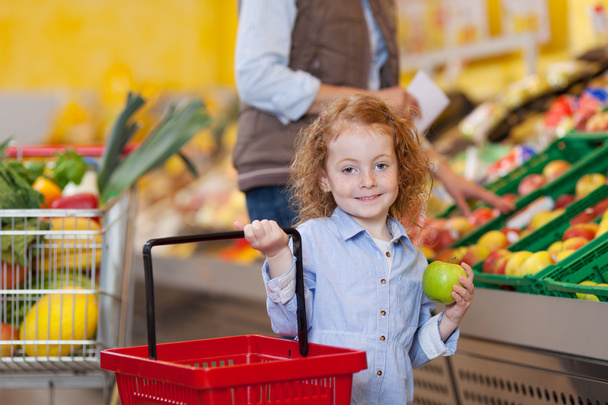 Girl Holding Shopping Basket And Apple At Grocery Store - Foto, afbeelding