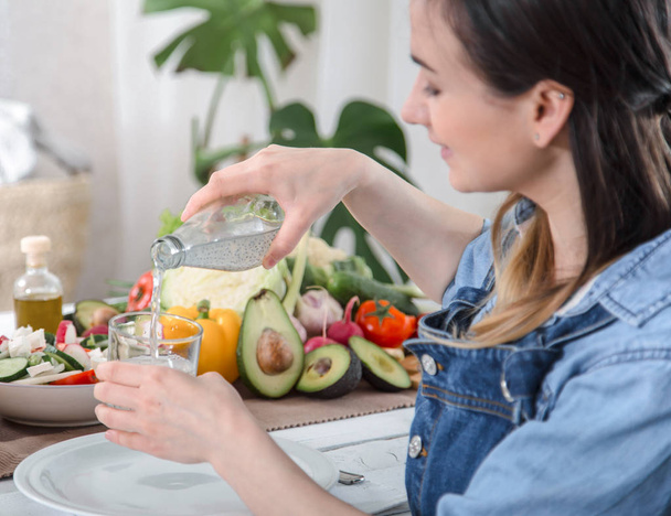 junge Frau trinkt Wasser am Tisch mit Gemüse - Foto, Bild