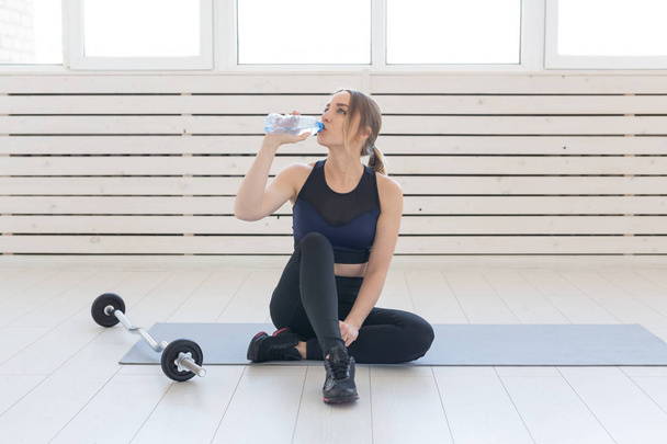 People, sport and fitness concept - young woman sitting with bottle of water on gym mat - Фото, зображення