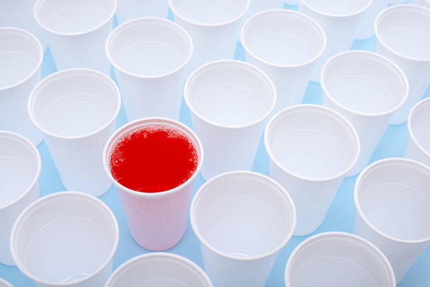 Copos vazios brancos de plástico descartáveis e um copo cheio de limonada vermelha
 - Foto, Imagem