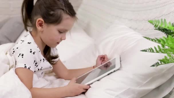 cute little child girl lies in bed uses digital tablet. - Video, Çekim