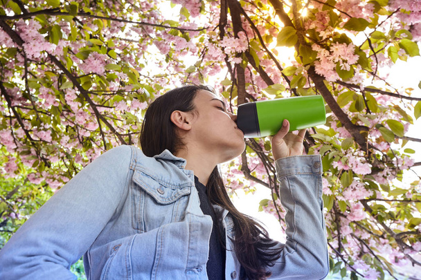 Young attractive girl drinking on the cherry tree street - Photo, Image
