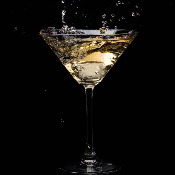 in a martini glass, vermouth ice falls, and splashes with drops on a black background - Фото, зображення