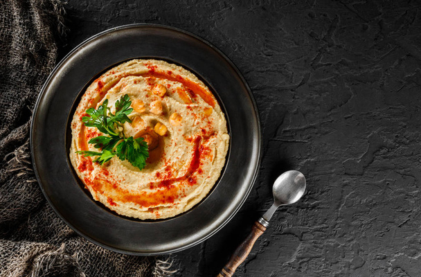 Chickpeas hummus with olive oil, paprika in a plate over dark stone background. Healthy vegan food, clean eating, dieting, top view - Foto, Bild