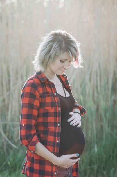 Mujer embarazada mirando su estómago al atardecer
 - Foto, Imagen