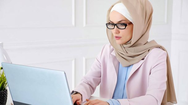 Mulher muçulmana nerd no hijab está trabalhando em um projeto de graduação bacharel digitando no laptop
 - Foto, Imagem