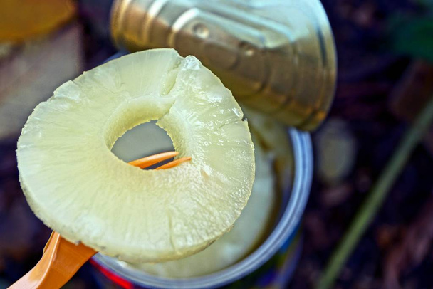 De vork trekt de ananas ring uit de ijzeren pot - Foto, afbeelding