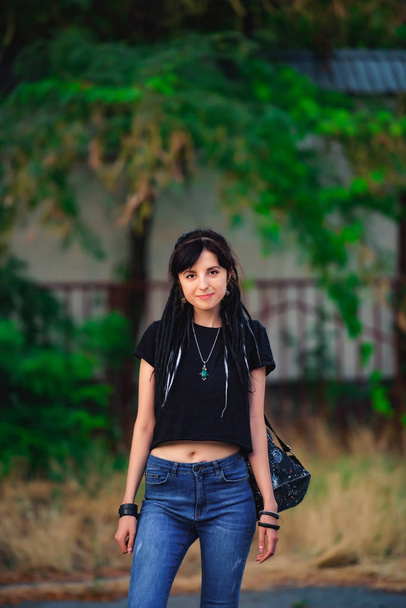 Девушка с черно-белыми дредами в парке. Молодая женщина с дредами. Девушка-модель в стиле хиппи в черной футболке и джинсах на открытом воздухе
 - Фото, изображение
