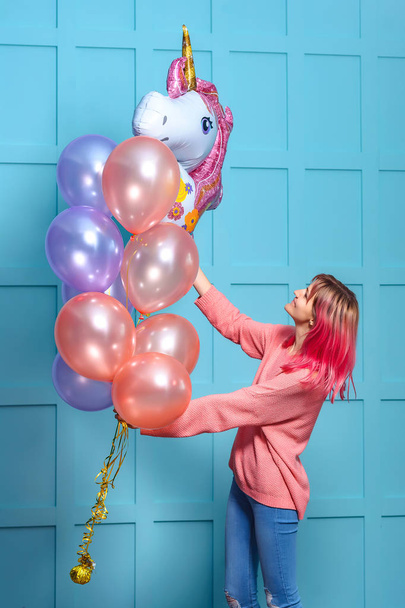 彼らの手に風船を持つピンクの髪を持つ女の子。ユニコーンのスタイルで誕生日パーティーを飾る。青い背景に風船とピンクの女の子. - 写真・画像