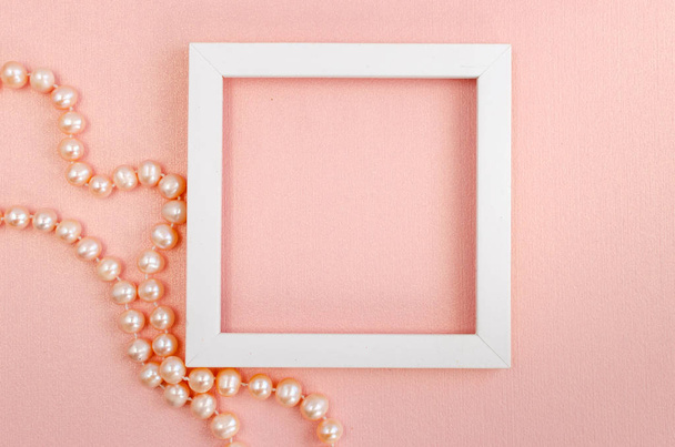 Biała kwadratowa ramka z perłowymi koralikami na różowej perłowej desce - Zdjęcie, obraz