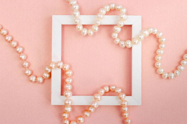 Bílý čtvercový rám s perlami na růžové perleťové desce - Fotografie, Obrázek