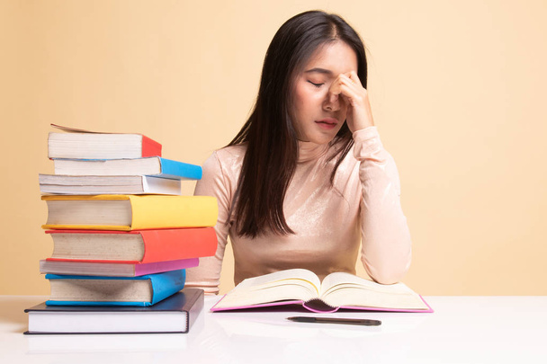 Mulher asiática exausta tem dor de cabeça ler um livro com livros na guia
 - Foto, Imagem