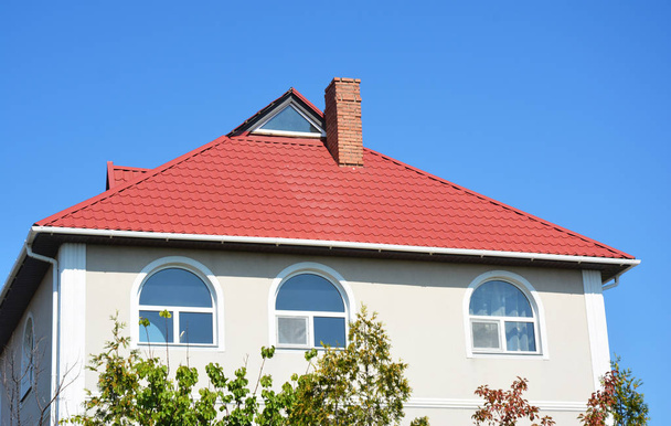 Modern ház tetőtéri ablak, piros fém tető és fehér műanyag eső ereszcsatorna. Tetőfedő munkák. - Fotó, kép