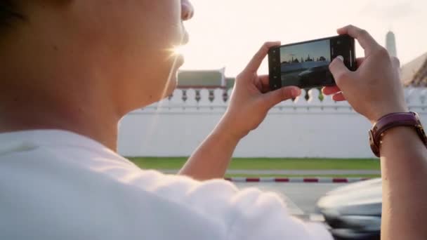 Reiziger Aziatische man met behulp van mobiele telefoon voor Neem een foto terwijl het doorbrengen vakantie reis in Bangkok, Thailand, Male geniet van een reis bij Amazing Landmark in Sunset. Lifestyle mannen reizen in stads concept. - Video