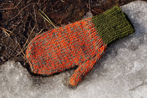una manopla de lana de colores yace sobre nieve blanca y tierra
 - Foto, imagen