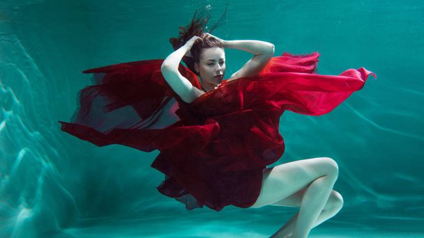 Mystical underwater portrait of a beautiful young woman in a red dress. Girl swimming underwater - Photo, image