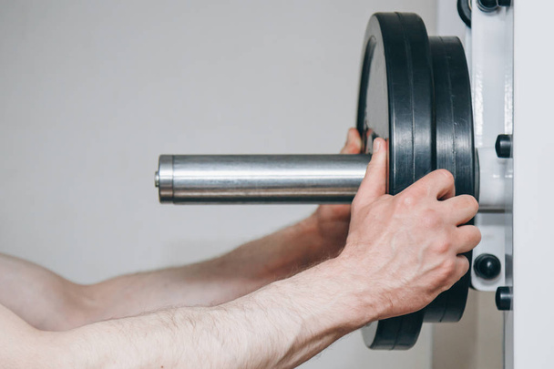 an athlete with big hands adds weight by the metal disks to the training apparatus in the training center. training equipment in the gym close-up - Foto, afbeelding