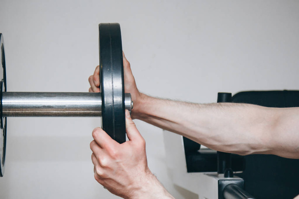 an athlete with big hands adds weight by the metal disks to the training apparatus in the training center. training equipment in the gym close-up - Φωτογραφία, εικόνα