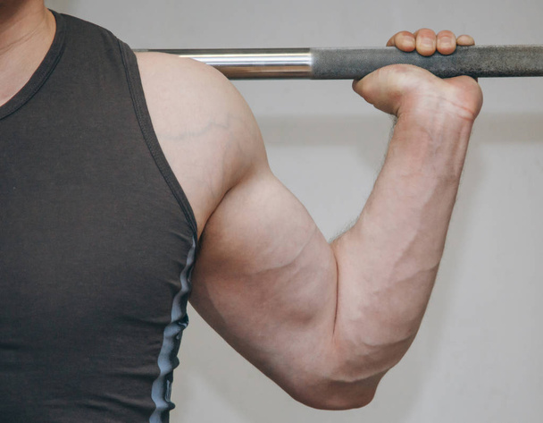 athlete with big hands holding a barbell bar in the training center. training tools in the gym close-up - Zdjęcie, obraz