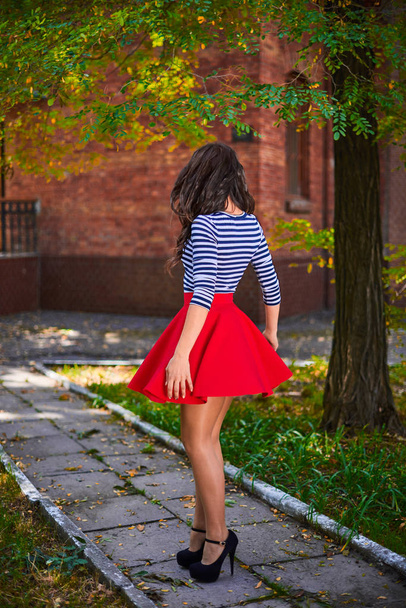 młoda brunetka z uśmiechem kręcąca się w parku. dziewczyna w czerwony spódnica taniec odkryty - Zdjęcie, obraz