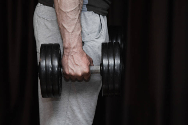 athlete trains biceps hands with dumbbells in the center of workouts on a black background. training tools in the gym close-up - Foto, afbeelding