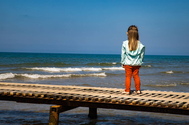 Una niña está de pie en el muelle del mar
. - Foto, Imagen