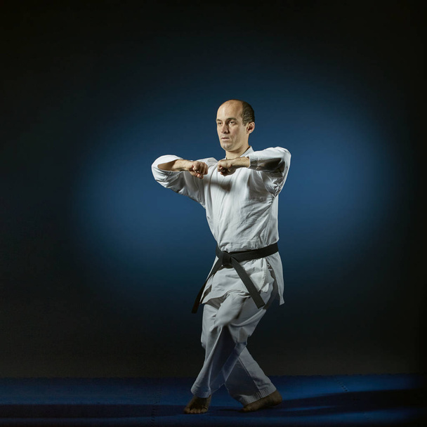Aktif atlet mavi tatami üzerinde resmi karate egzersizleri yapıyor - Fotoğraf, Görsel