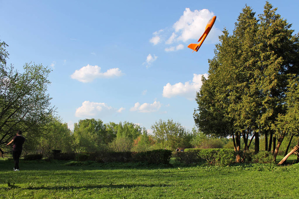 Orange foam airplane floating in the air against the background of white clouds and blue sky - Foto, afbeelding