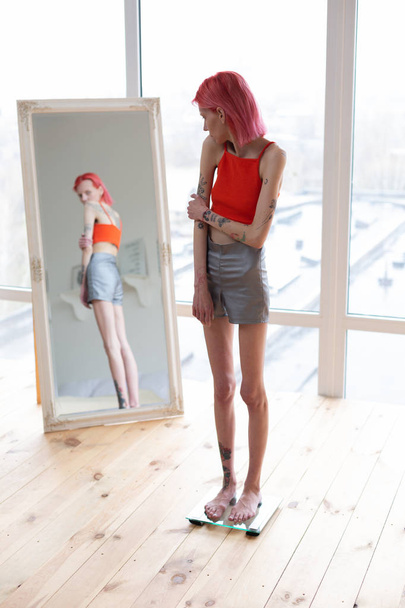 スケールに立って鏡を見る食欲不振の女性 - 写真・画像