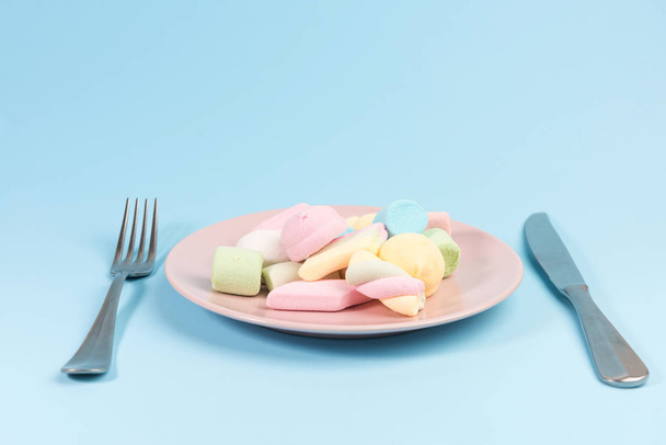 Plate with marshmallow, fork, knife  isolated on blue background. - Foto, Imagen