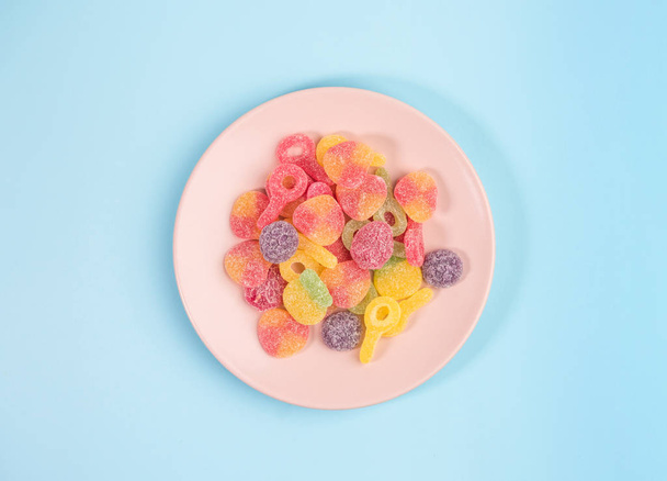 Pink plate with gummy candies on blue background. Top view. - Photo, image