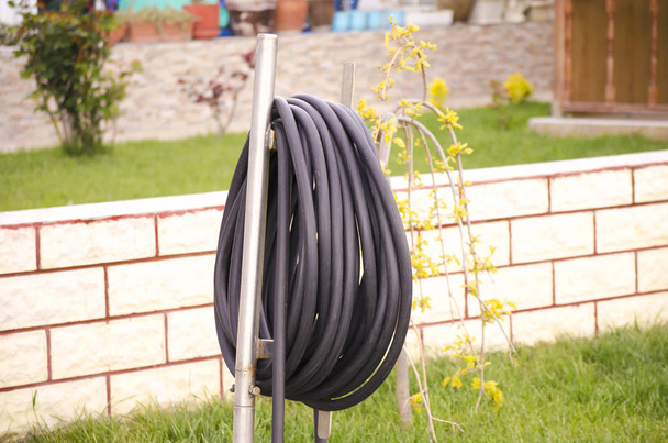 Black garden hose for watering is wound on a special stand. Stand for a hose in the garden, on the green grass. Garden at home on a summer sunny day. Selective focus image. - Photo, Image
