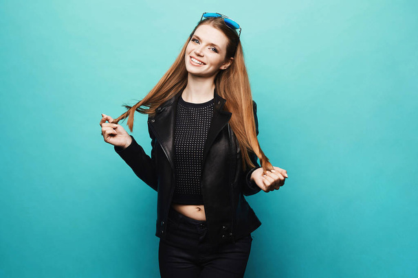 Young blonde model woman in a stylish black leather jacket and in black jeans posing at the light blue background, isolate - Valokuva, kuva