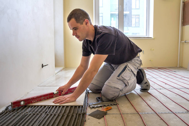 Молодой рабочий плитки установки керамической плитки с помощью рычага на cemen
 - Фото, изображение