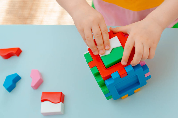 gros plan des mains de l'enfant collecter puzzle trieur. Cube avec des formes géométriques insérées et des blocs en plastique coloré. - Photo, image