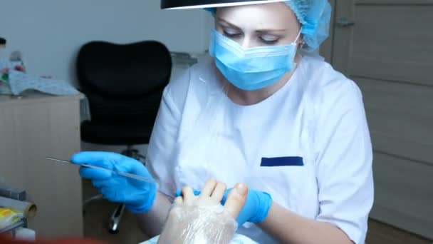 Pedicure Master in een masker zagen een nagel plaat en bereidt zijn nagels voor gel Polish, voeten verpakt in plastic wrap - Video