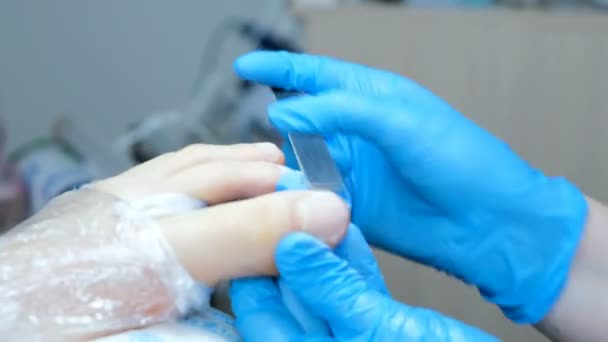 Pédicure maître scie la plaque à ongles sur les jambes fermer, les pieds sont enveloppés dans une pellicule plastique
 - Séquence, vidéo