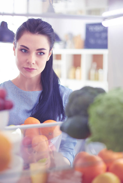 Улыбающаяся женщина достает свежие фрукты из холодильника, концепция здоровой пищи - Фото, изображение