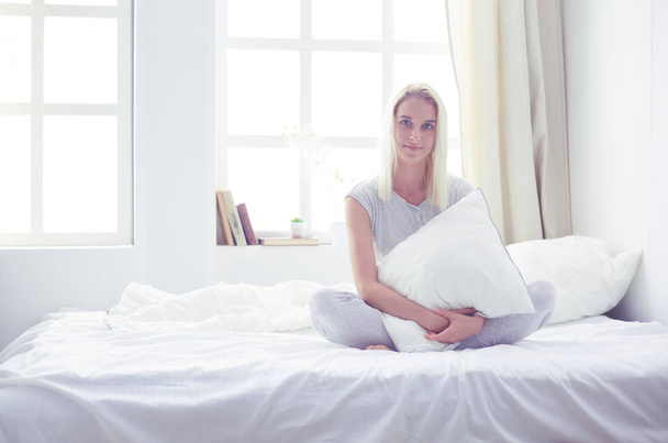 sevimli kadın yatağında otururken bir yastık holding - Fotoğraf, Görsel