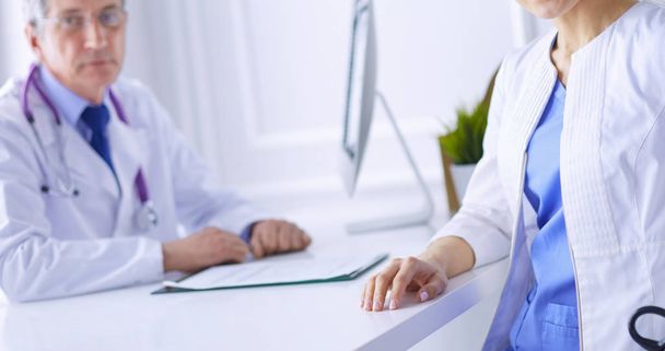 Un médico sonriendo a la cámara con su compañero de sexo masculino en la parte trasera de la sala de consulta en el hospital - Foto, Imagen