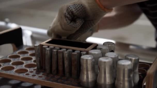 Ruční rukavice přebírá cylindric kovové kolíky z dřevěné krabice s kulatými otvory. - Záběry, video
