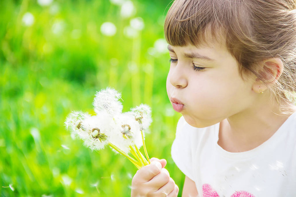 girl blowing dandelions in the air. selective focus. - Photo, Image