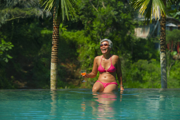 natural lifestyle portrait of attractive and happy middle aged Asian woman relaxed at tropical resort infinity simming pool with jungle background enjoying a drink relaxed - Foto, Imagem