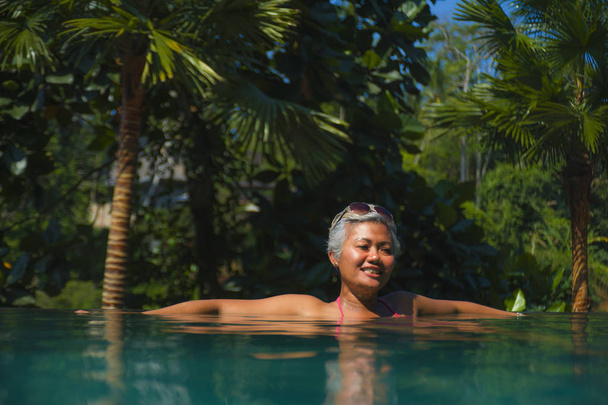 attractive and happy middle aged Asian woman relaxed at tropical resort infinity swimming pool with jungle background enjoying relaxed in luxury holidays trip - Foto, Imagem