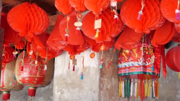Papieren lantaarns op armoedig gebouw. Rode papieren lantaarns opknoping op het plafond van verweerde betonnen tempel gebouw op zonnige dag in oosterse land. traditionele decoratie - Video