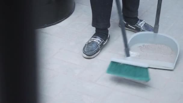 Someone wearing sneakers is sweeping debris off of white floor into dustpan. - Footage, Video