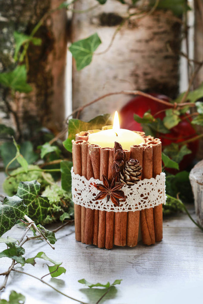 Candle decorated with cinnamon sticks, moss, ivy leaves and wood - Fotó, kép