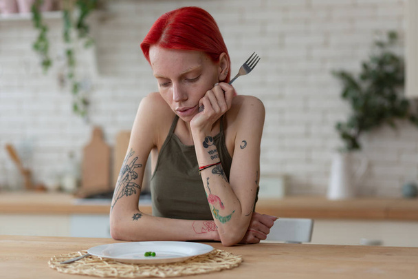 Woman with bulimia holding fork and looking at plate with peas - Fotografie, Obrázek