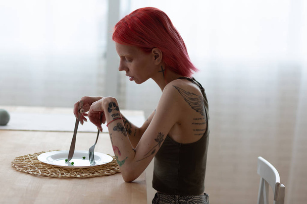 Anorexic woman with tattooed back sitting in front of empty plate - Photo, image